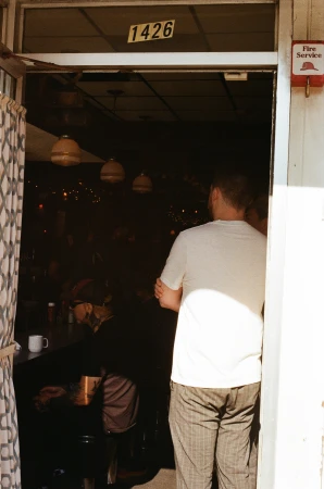 Adult male entering dimly lit restaurant through open doorway, patron sitting at bar, overhead lighting visible inside.