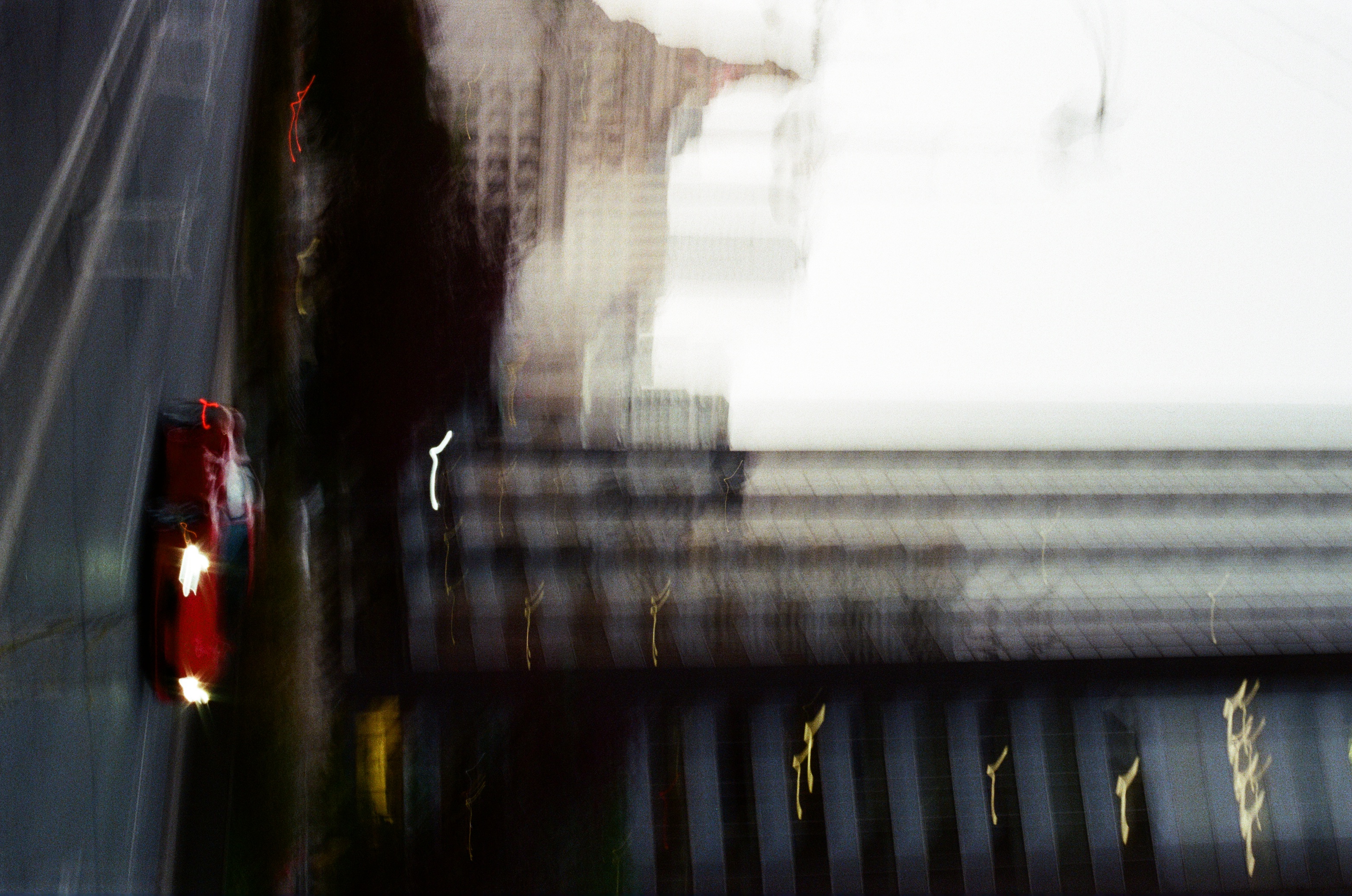 Red car races down a city street with tall buildings in the background, motion blur effect creates a sense of speed.