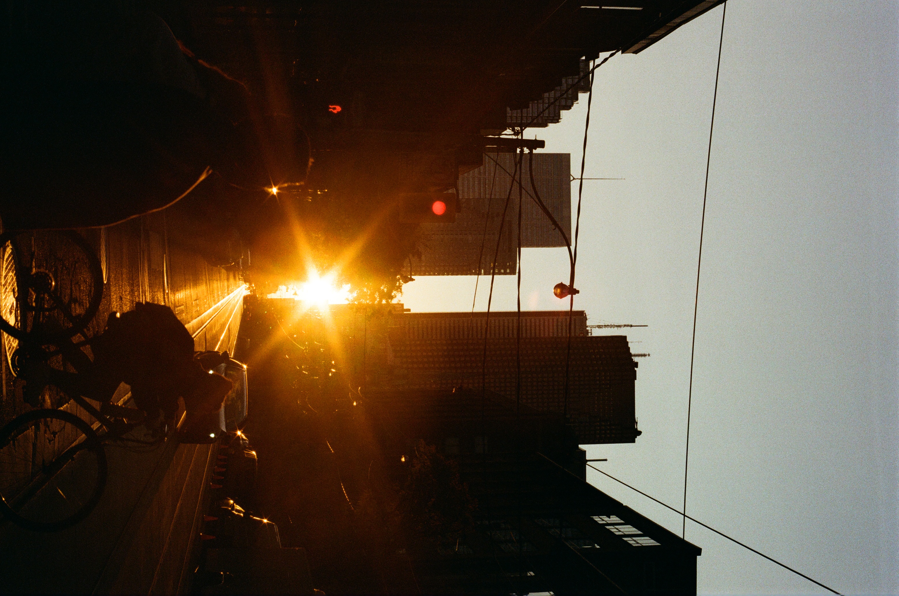 Urban sunrise silhouette features cyclist on city street, buildings, power lines and bright starburst sun creating visual interest.