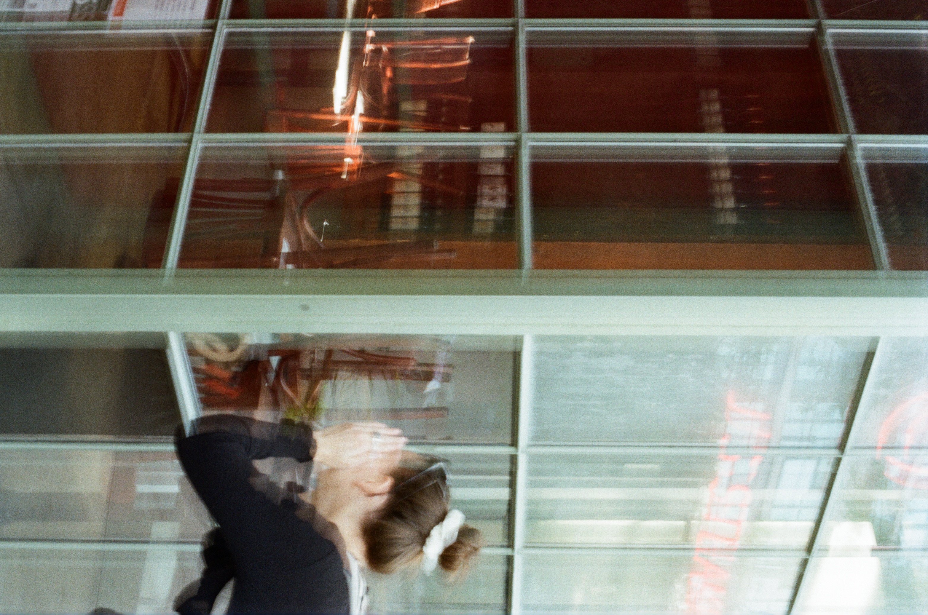 Woman stands outside a building with large windows, her hands near her face. The interior of the building is visible through the glass.