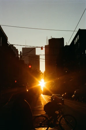 Silhouetted cyclist riding down a city street directly toward a brilliant golden hour sunset between towering skyscrapers.