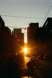 Silhouetted cyclist riding down a city street directly toward a brilliant golden hour sunset between towering skyscrapers.