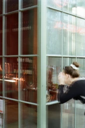 A woman with her hair in a bun peers through a large multi-paned glass window of a closed restaurant storefront in Paris.