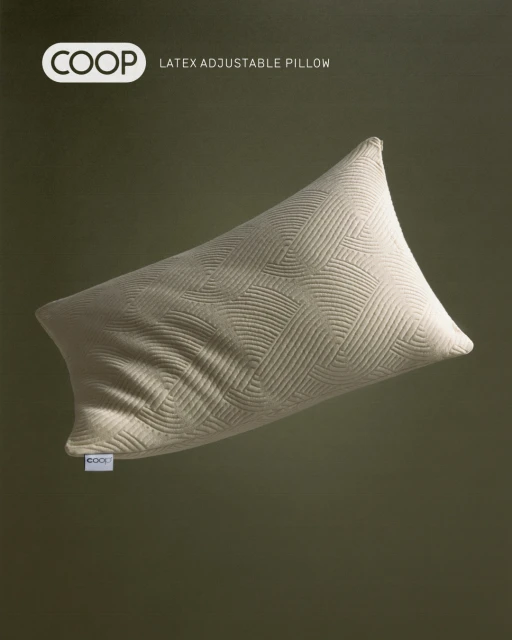 Beige Coop latex adjustable pillow with a geometric pattern is against a green backdrop in a studio product shot for advertising.