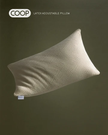 Beige Coop latex adjustable pillow with a geometric pattern is against a green backdrop in a studio product shot for advertising.