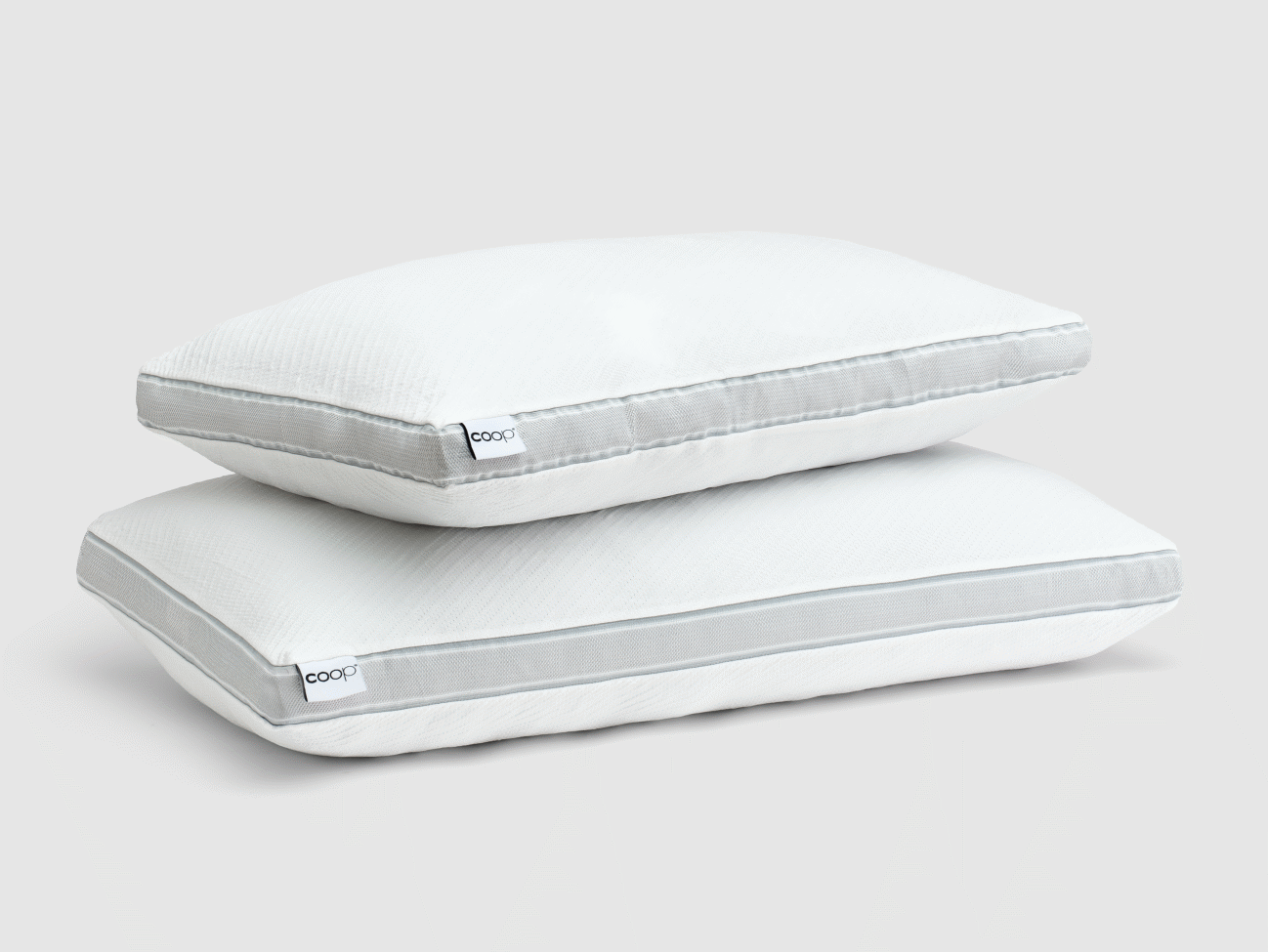 Two white pillows stacked on top of each other in a studio setting, showcasing bedding and home decor.