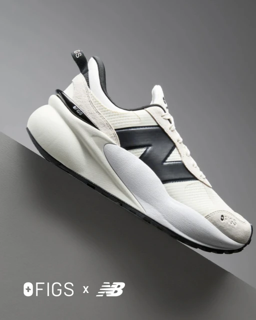 Studio shot of a New Balance x OFIGS sneaker featuring black logo and white colourway against a gradient grey background.
