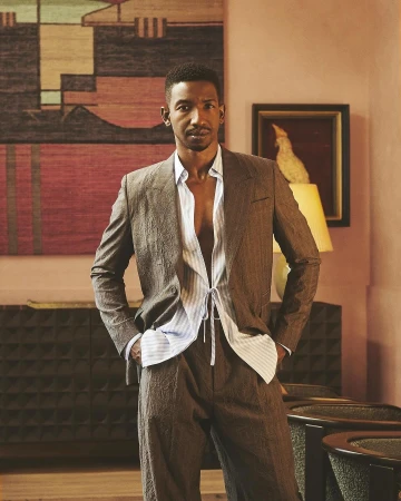 Man wearing a brown textured suit jacket over a light blue striped unbuttoned shirt photographed indoors by Ssam Kim.