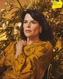 Neve Campbell in a gold patterned dress posing amidst gilded botanical foliage by photographer Ssam Kim.