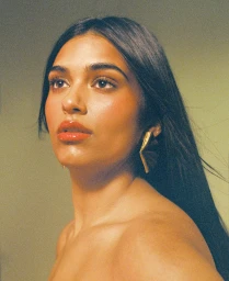 Close-up portrait of a woman with long dark hair, glossy lips, and gold geometric earrings against a soft neutral background