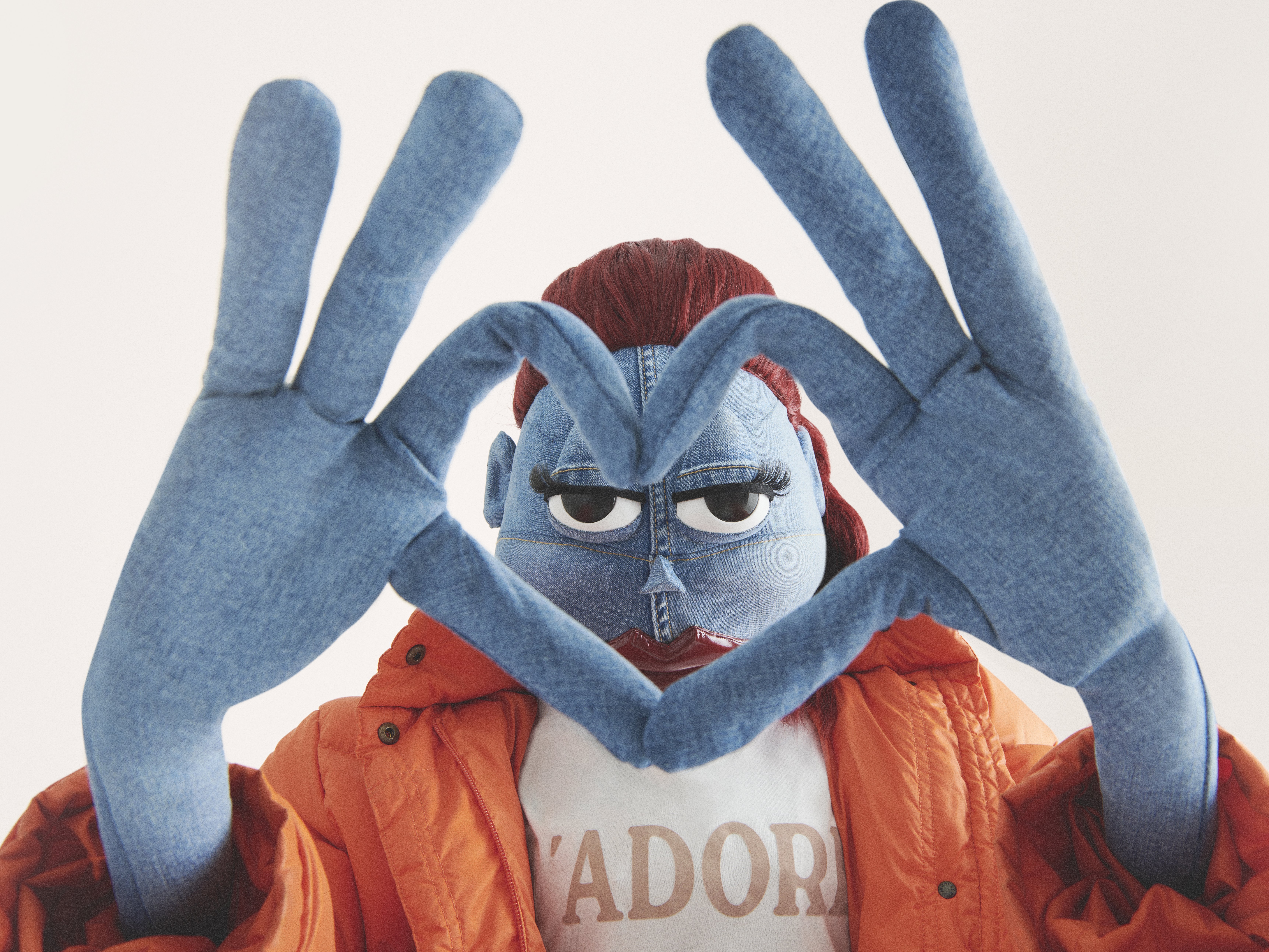 Person crafted from denim in bright orange jacket, making a heart with denim hands, creating a whimsical, surreal and fashionable image.