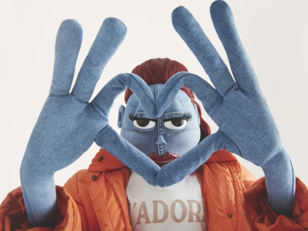 Person crafted from denim in bright orange jacket, making a heart with denim hands, creating a whimsical, surreal and fashionable image.