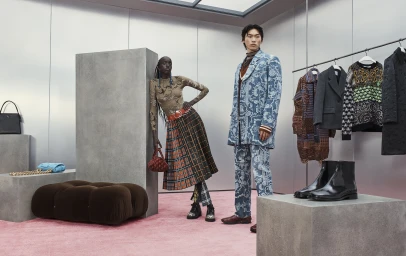 Two fashion models posing in designer clothing inside a modern showroom featuring concrete pedestals and pink carpet.