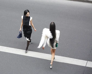 Two women walking across an asphalt street with white road markings, viewed from a high angle.