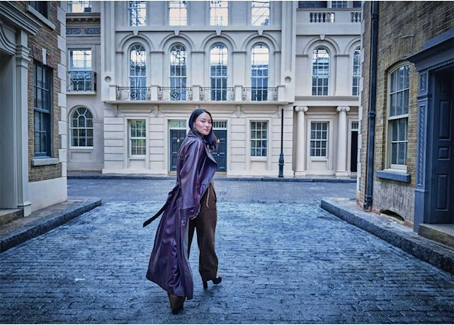 A woman in a long coat walks on a cobblestone street in an urban environment surrounded by classic buildings during the daytime.