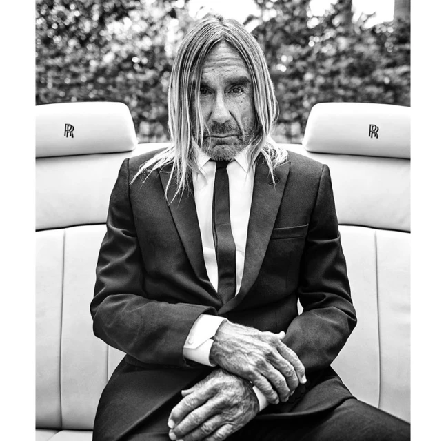 Black and white portrait of an adult male in a suit, sitting in a car with leather seats, with trees visible in the background.