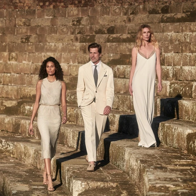 Two women and a man wearing formal attire walk down stone steps in an outdoor setting, bathed in natural light.