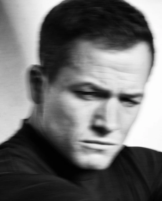Close-up portrait of actor Daniel Craig with a serious expression, wearing a black suit and bow tie, against a dark background.