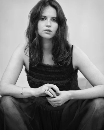 Portrait of Felicity Jones in a dark textured dress with hands clasped, shot in monochrome by Gavin Bond