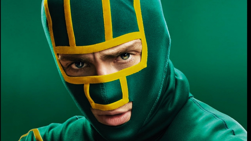 Close-up of a man wearing a green and yellow superhero-style mask against a solid green background, providing a dynamic and vibrant composition.