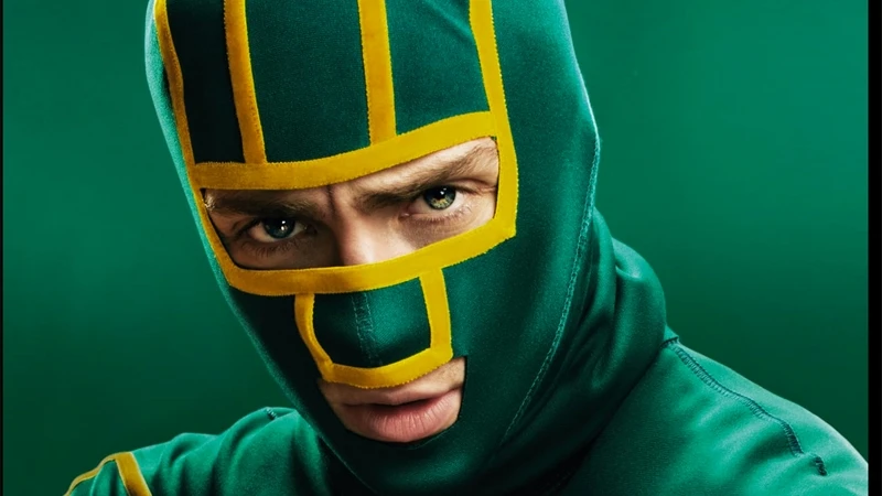 Close-up of a man wearing a green and yellow superhero-style mask against a solid green background, providing a dynamic and vibrant composition.