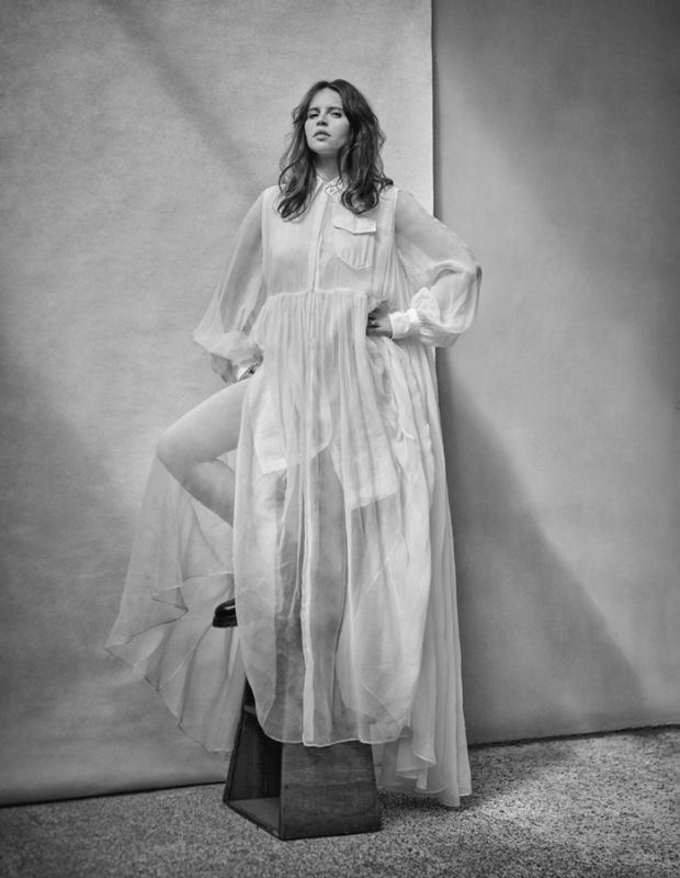 Monochrome portrait of a woman in a sheer white dress posing in a photo studio, with soft lighting and a textured backdrop.