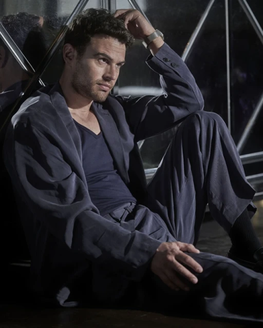Portrait of an adult male wearing a suit with curly hair, hand on head, looking away with a dark background and window reflection.