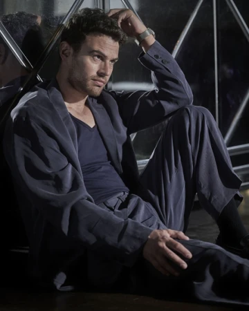 Portrait of an adult male wearing a suit with curly hair, hand on head, looking away with a dark background and window reflection.