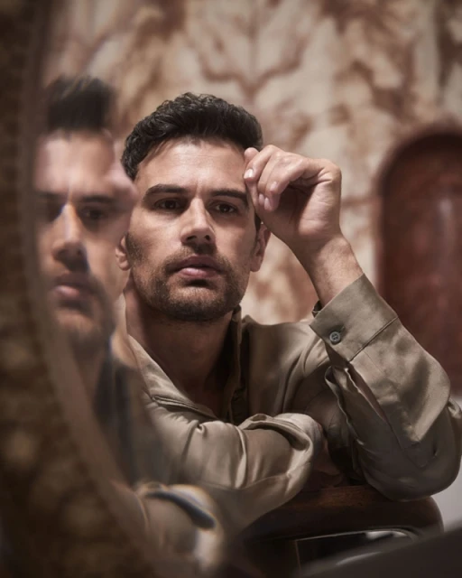Portrait of a brunette adult male in a collared shirt, looking at the camera, reflected in a mirror with a patterned backdrop.