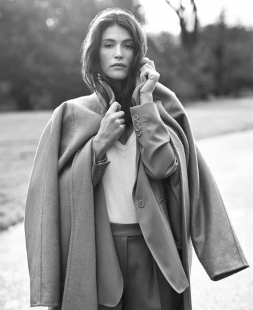 Monochrome portrait of a woman wearing a tailored blazer and coat draped over her shoulders outdoors.