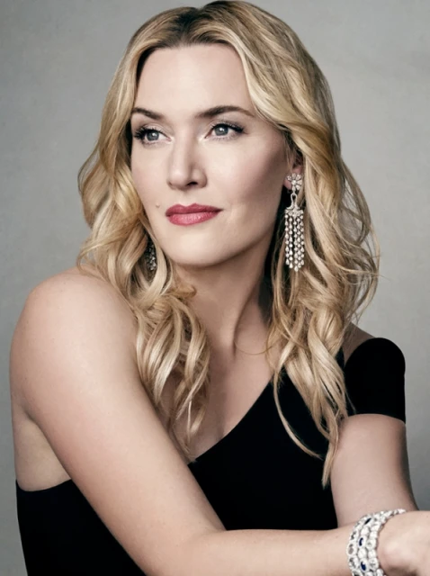 Glamorous portrait of a blonde woman with sparkling jewelry, wearing a black dress against a soft, neutral background in a photo studio.