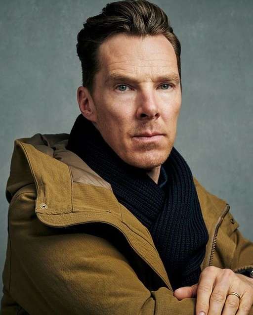 Portrait of adult male wearing a tan jacket and black scarf, gazing directly at the camera with a neutral facial expression.