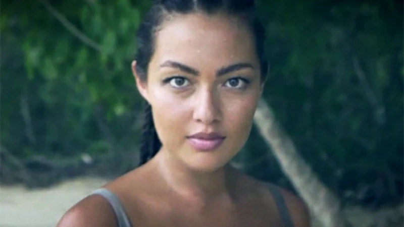 Close-up portrait of a woman with dark hair and grey eyes against a blurred green forest background