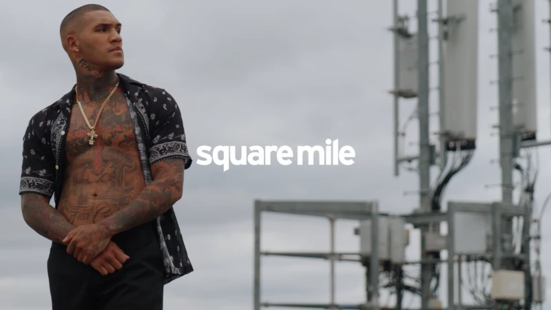 Tattooed man in open shirt with necklace looks left against a grey sky with radio towers. Text reads 'square mile'.