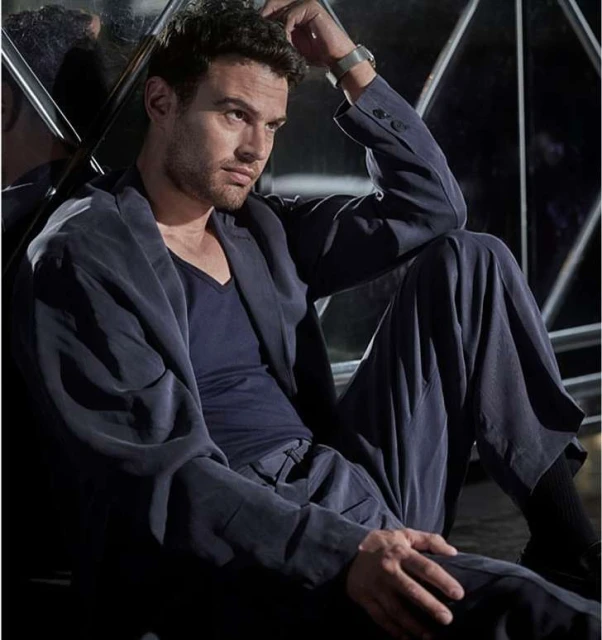 Portrait of a handsome man sitting on the floor in a suit, striking a thoughtful pose in front of a reflective background.