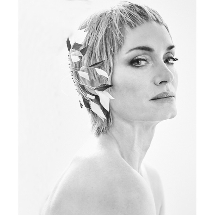 Black and white portrait of an adult woman with short hair, light skin, wearing patterned headwear, against a bright white backdrop.