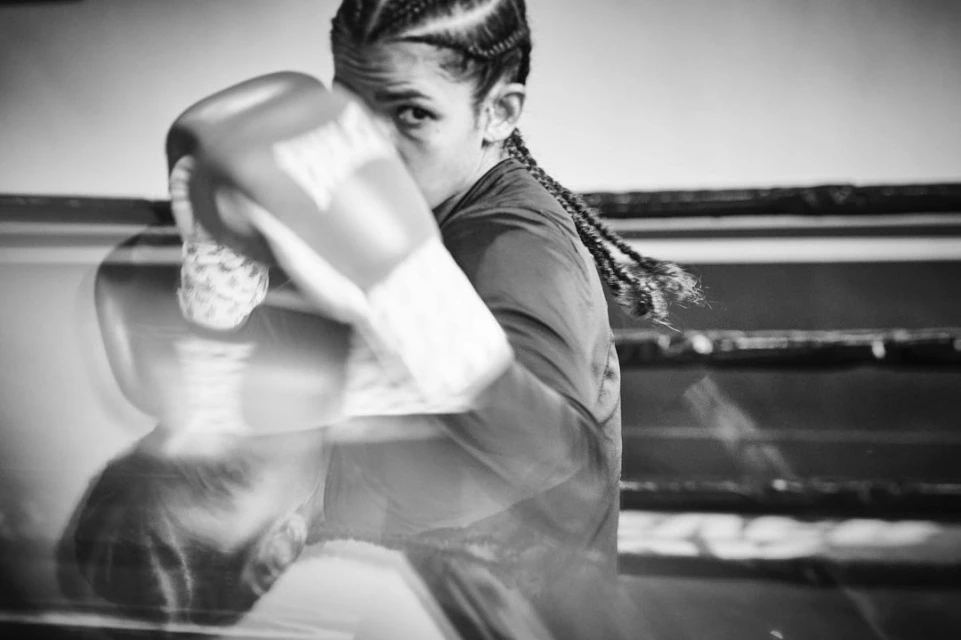 Monochrome shot of a female boxer in motion, wearing Everlast gloves, showcasing athleticism and determination in an indoor setting.