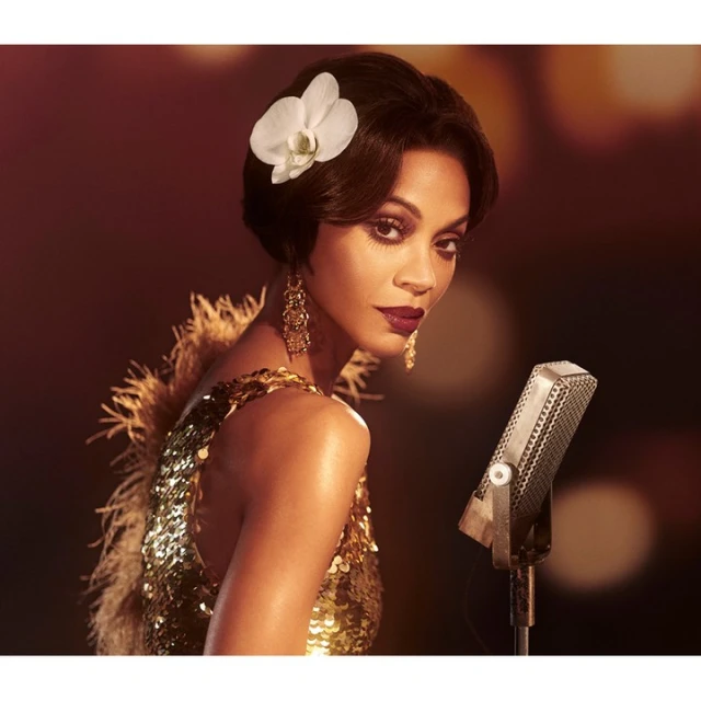 Glamorous African American woman with a flower in her hair sings into a vintage microphone while wearing a gold, sequined dress.