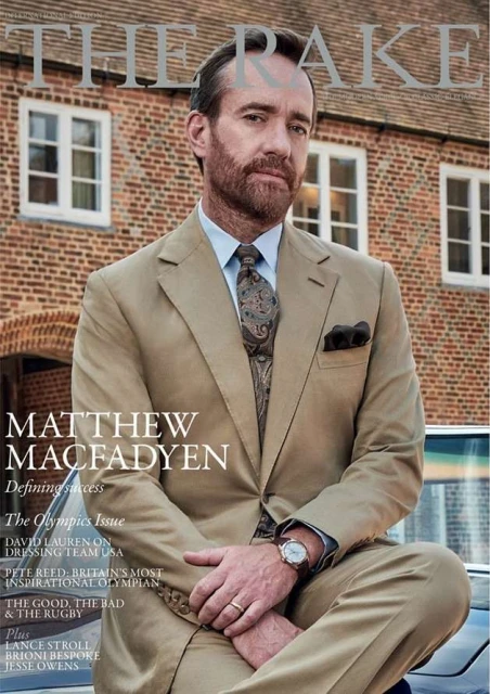 Matthew Macfadyen on the cover of The Rake magazine, wearing a tan suit and patterned tie, posing in front of a brick building.