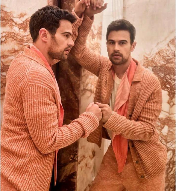 Close-up of actor Theo James leaning against a marble pillar in a peach-toned suit, reflected in the pillar. Fashion editorial photography.