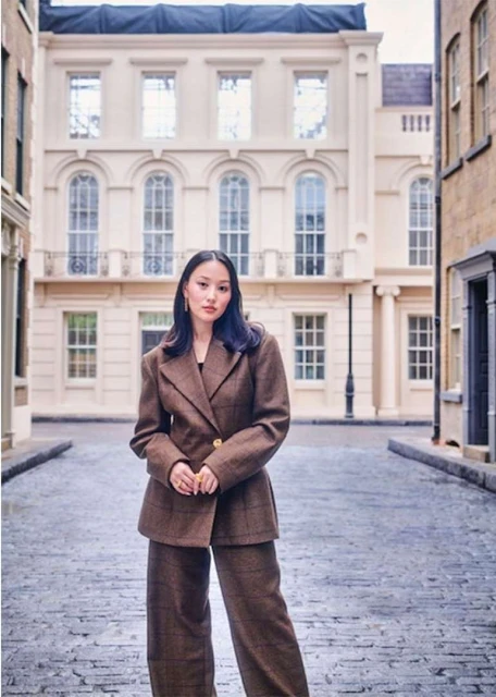Woman in a brown pantsuit stands on a cobblestone street in front of a cream-colored building with arched windows and a black lamppost.