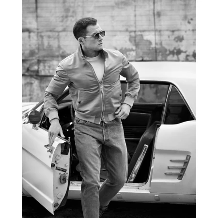 Black and white portrait of a man in a jacket and jeans exiting a white car in an urban setting.