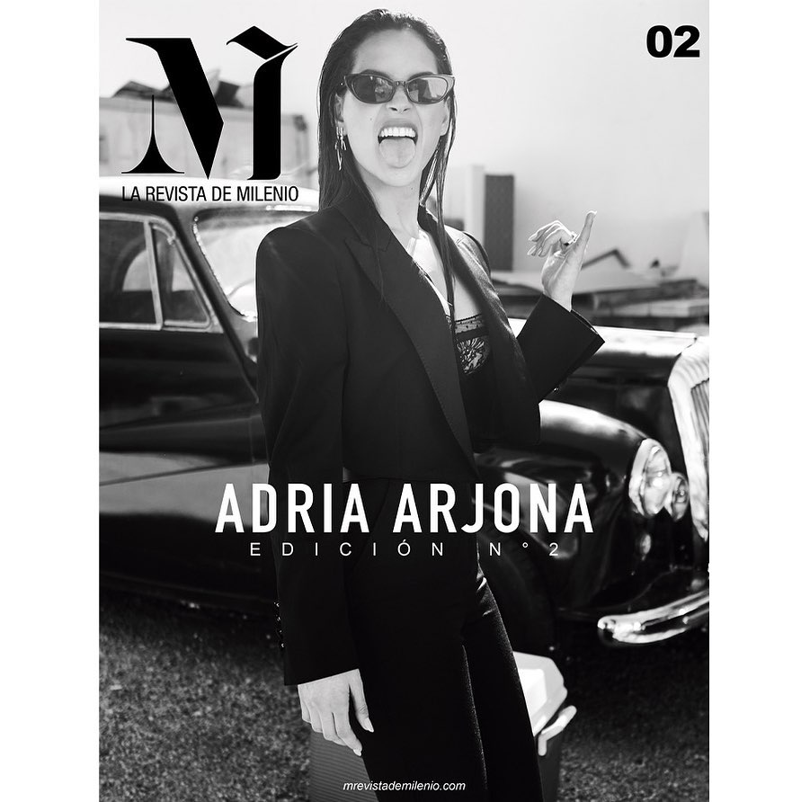 Magazine cover featuring a woman in a black blazer, sunglasses, and her tongue out, standing in front of a black classic car.