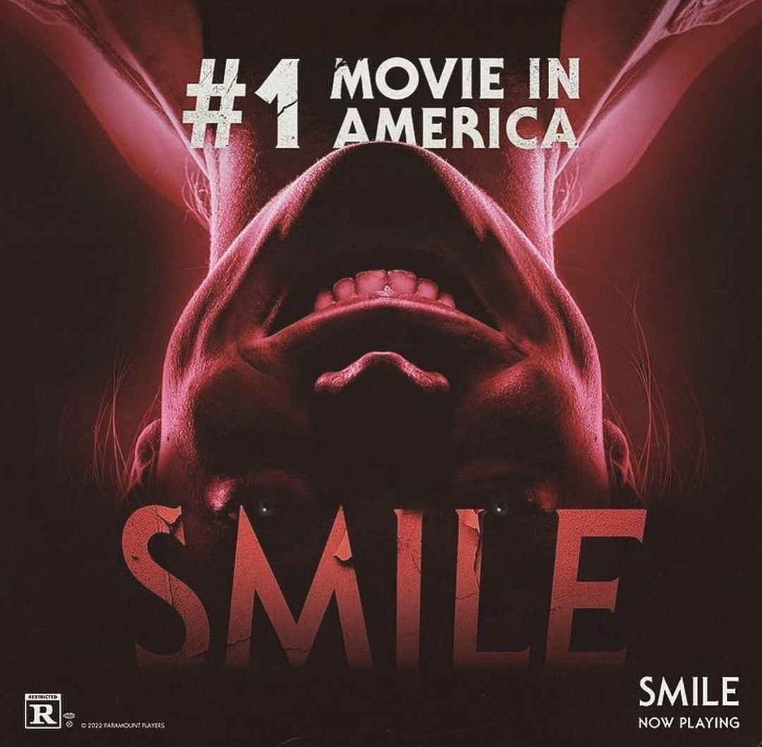 Movie poster featuring an upside-down woman's face, the text '#1 Movie in America', and the movie title 'Smile' in cracked lettering.