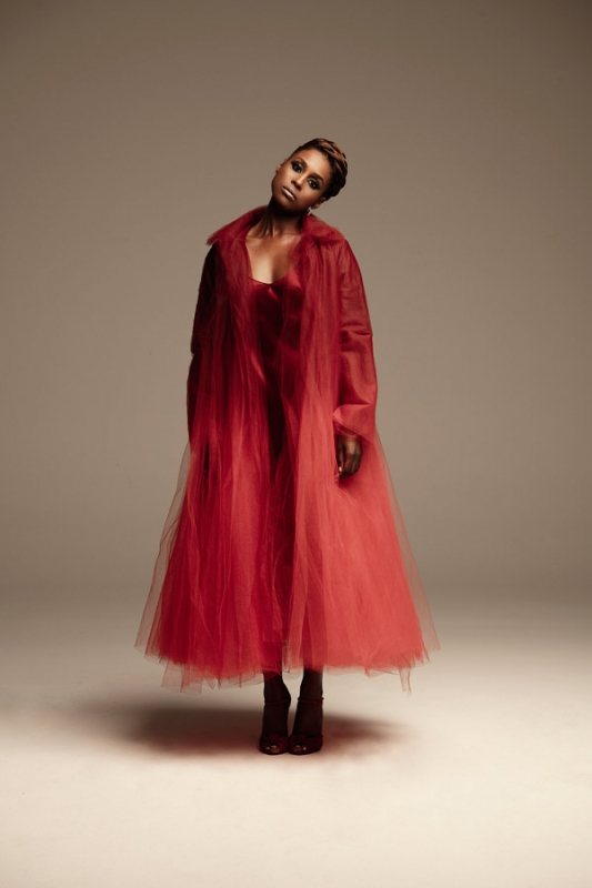 Elegant woman in red tulle dress and coat, striking a confident pose in a photo studio, fashion portrait with soft lighting.