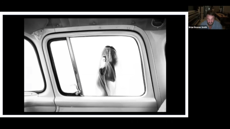 Black and white photo of a woman with a veil, seen through the window of a vintage van, creating a sense of mystery and timelessness.