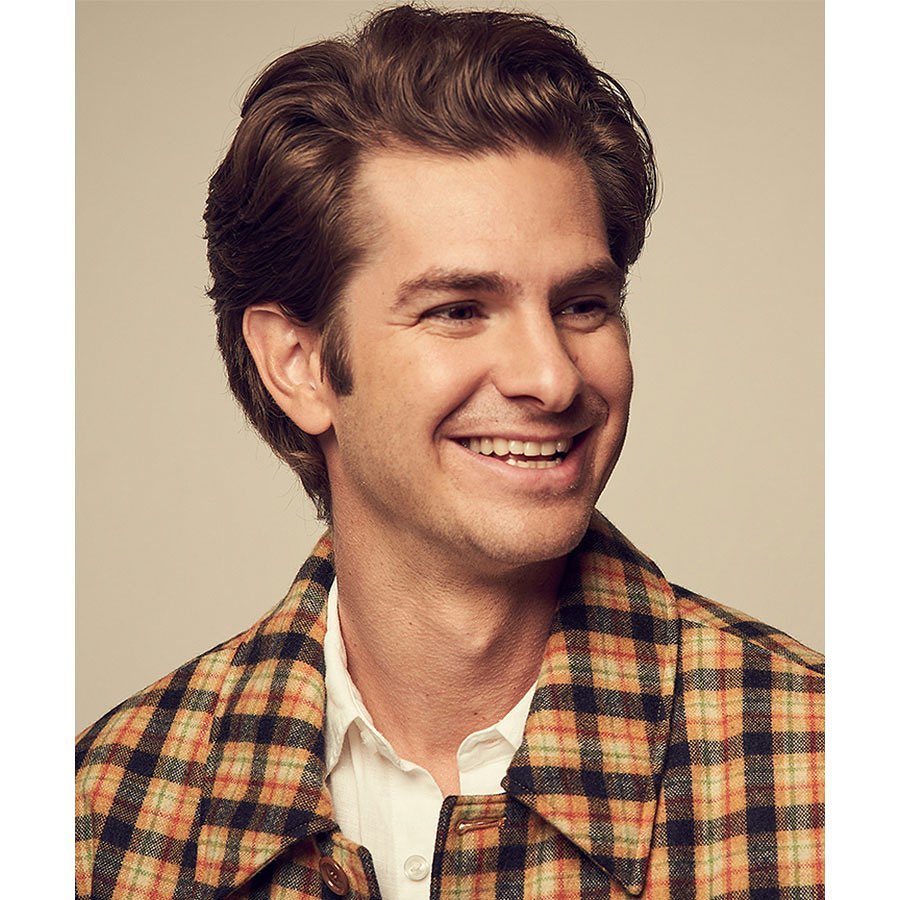 Headshot of a smiling adult male with medium brown hair, wearing a plaid jacket, against a neutral background. Portrait orientation.