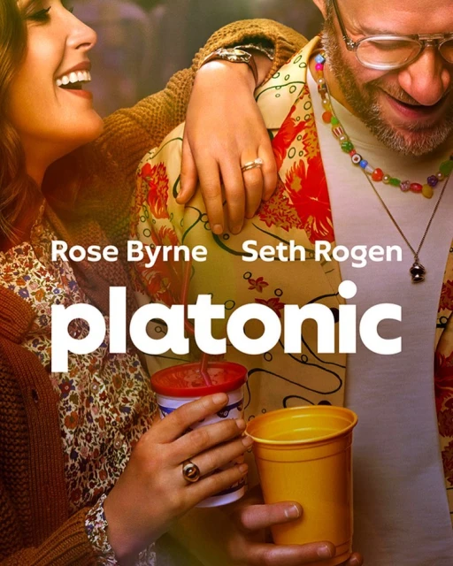Promotional shot of Rose Byrne and Seth Rogen embracing, showcasing the show "Platonic." Both hold drinks in a brightly lit scene.