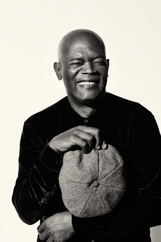 Monochrome portrait of a smiling adult man holding a flat cap against a neutral backdrop in a photography studio setting.