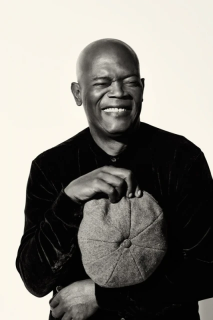 Monochrome portrait of a smiling adult man holding a flat cap against a neutral backdrop in a photography studio setting.